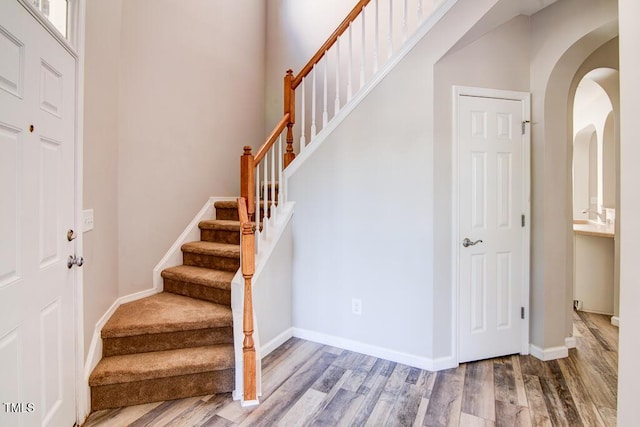 foyer featuring baseboards, stairs, wood finished floors, and arched walkways