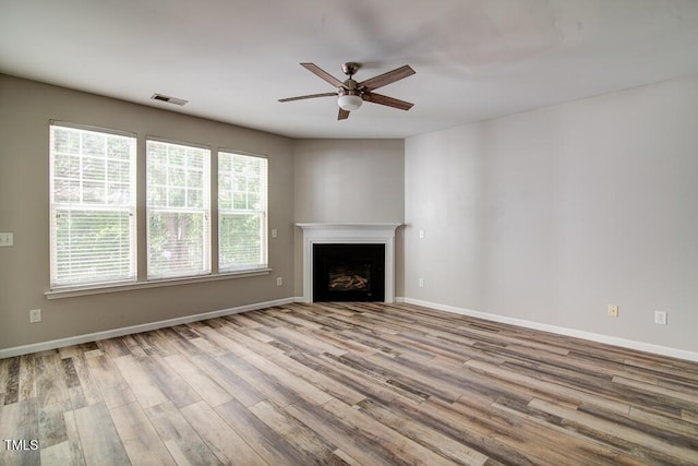 unfurnished living room with ceiling fan, a fireplace, baseboards, wood finished floors, and visible vents
