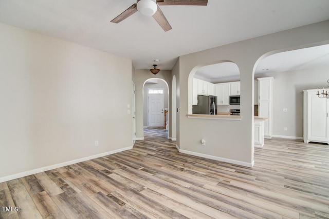 unfurnished living room with a ceiling fan, baseboards, light wood-style flooring, and arched walkways