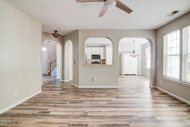 unfurnished living room featuring arched walkways, ceiling fan with notable chandelier, and light wood finished floors