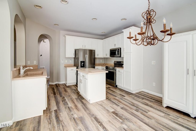 kitchen with a notable chandelier, a sink, light countertops, arched walkways, and stainless steel appliances