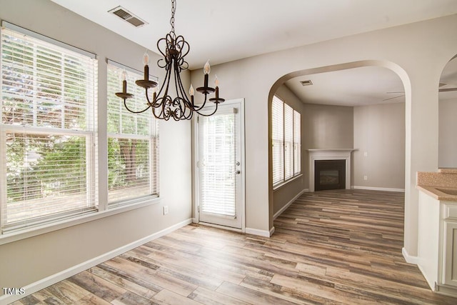 unfurnished dining area with arched walkways, baseboards, wood finished floors, and visible vents