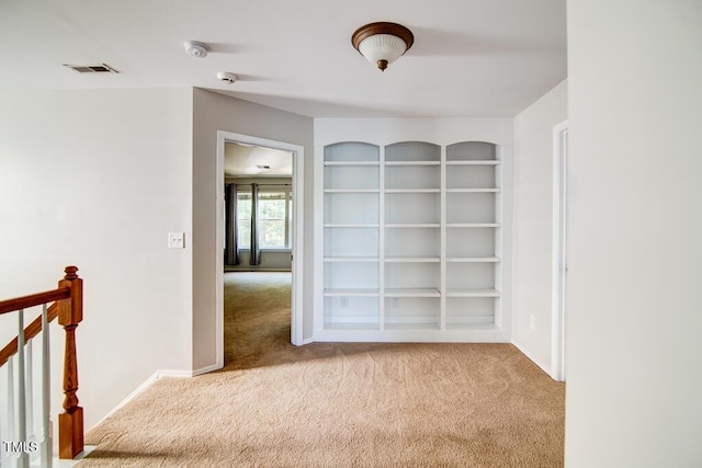 spare room with carpet flooring, baseboards, visible vents, and built in shelves