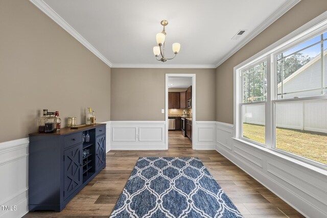dining area with ornamental molding, wainscoting, wood finished floors, and a notable chandelier