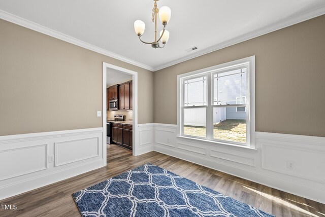 dining area with visible vents, crown molding, wainscoting, wood finished floors, and an inviting chandelier