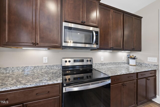 kitchen with stainless steel microwave, dark brown cabinetry, light stone countertops, and black range with electric stovetop