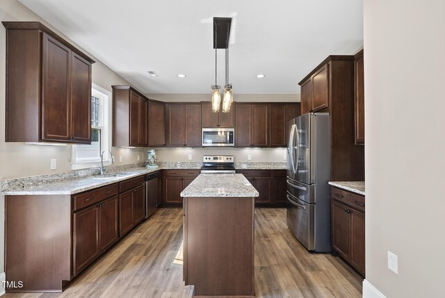 kitchen with appliances with stainless steel finishes, a center island, light wood-type flooring, a sink, and light stone counters