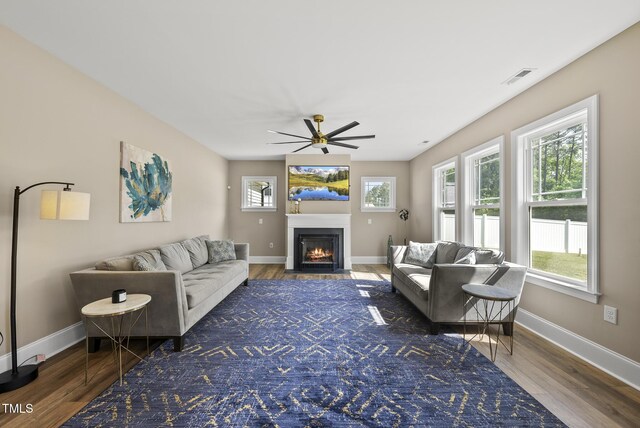 living area with ceiling fan, visible vents, a fireplace with flush hearth, wood finished floors, and baseboards