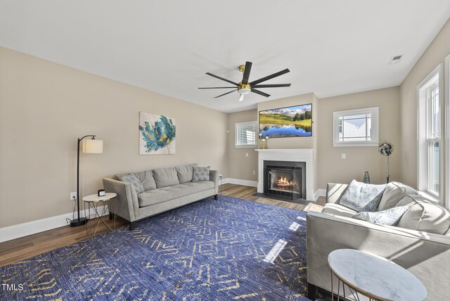 living area featuring visible vents, wood finished floors, baseboards, ceiling fan, and a fireplace with flush hearth