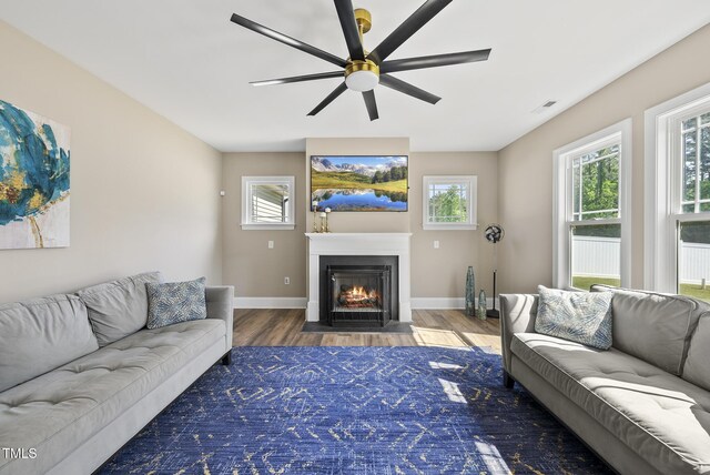 living area with ceiling fan, baseboards, a fireplace with flush hearth, wood finished floors, and visible vents