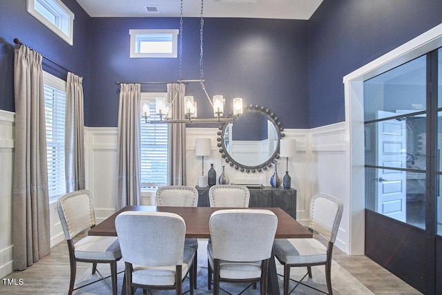 dining area featuring an inviting chandelier, wainscoting, wood finished floors, a towering ceiling, and visible vents