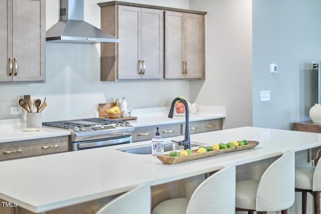 kitchen with a sink, stainless steel range with gas stovetop, a kitchen breakfast bar, light countertops, and wall chimney exhaust hood