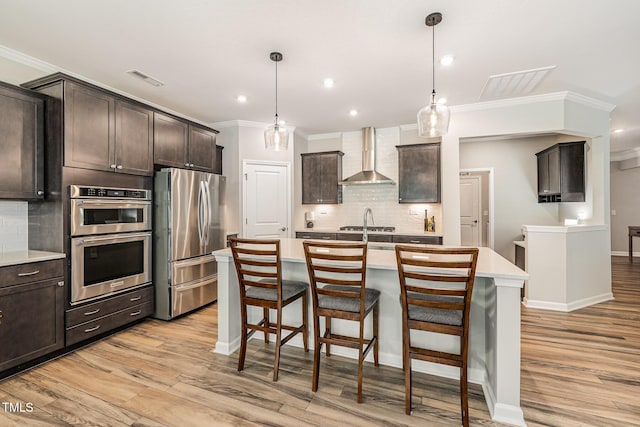 kitchen with appliances with stainless steel finishes, wall chimney range hood, crown molding, backsplash, and light wood-style floors
