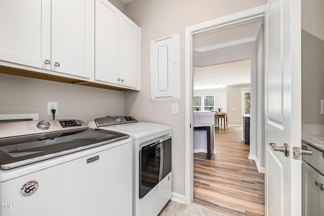 clothes washing area with washing machine and clothes dryer, cabinet space, baseboards, and light wood finished floors
