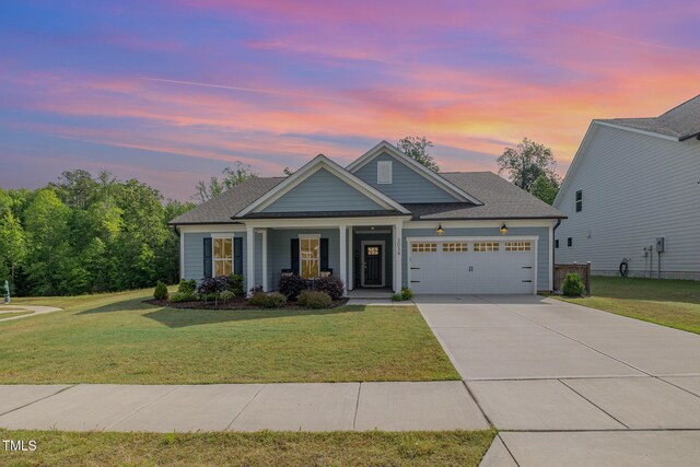view of front facade featuring an attached garage, covered porch, a yard, and driveway