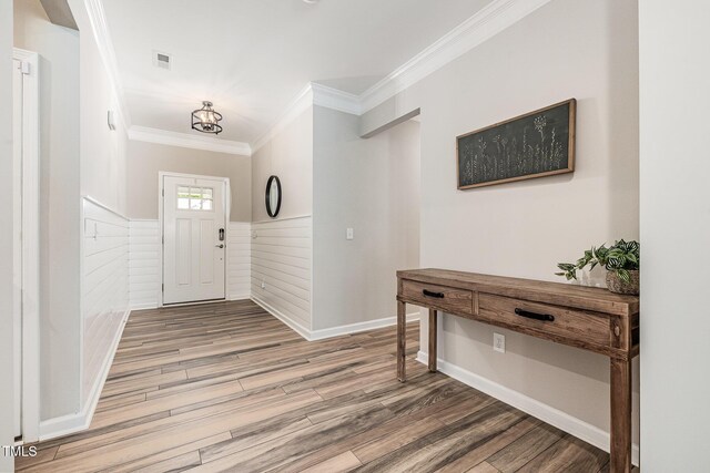 foyer entrance with crown molding, a wainscoted wall, and wood finished floors