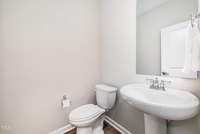 half bath featuring wood finished floors, toilet, baseboards, and a sink