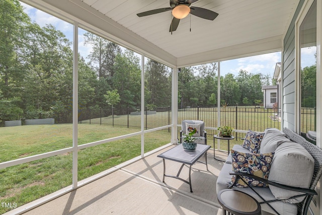 sunroom featuring a ceiling fan and view of wooded area