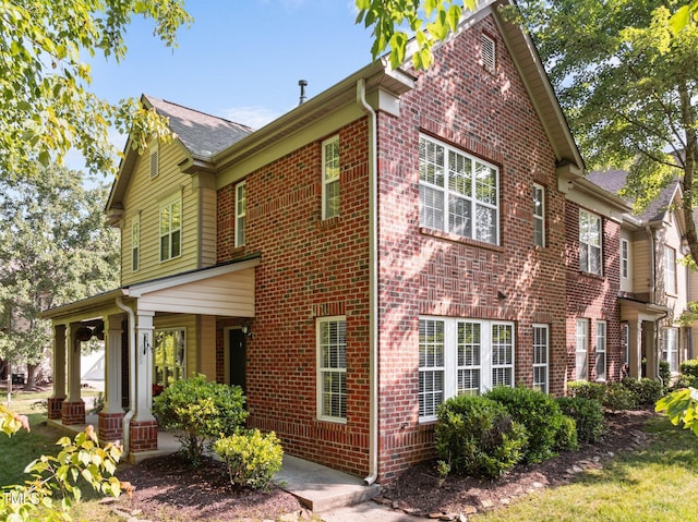 view of home's exterior with covered porch, brick siding, and roof with shingles
