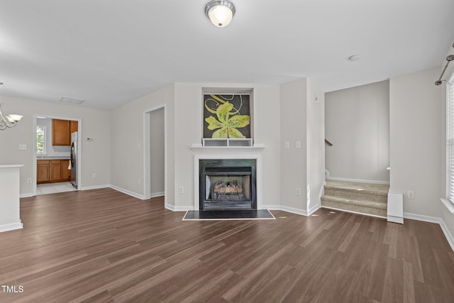 unfurnished living room featuring an inviting chandelier, dark wood-style floors, stairway, and a high end fireplace