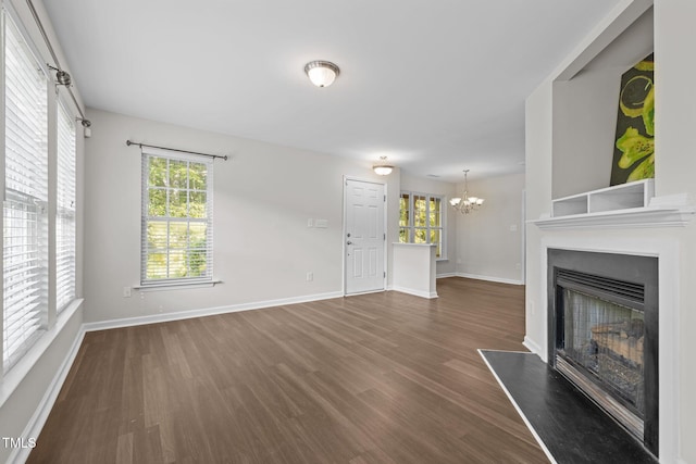 unfurnished living room featuring an inviting chandelier, a fireplace with raised hearth, wood finished floors, and a wealth of natural light