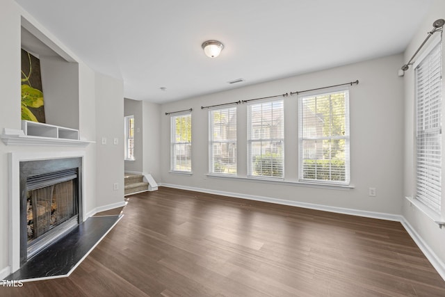unfurnished living room with a fireplace with raised hearth, wood finished floors, and a wealth of natural light
