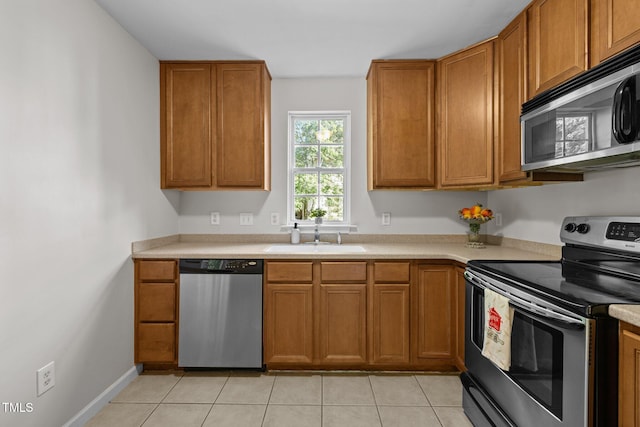 kitchen with light countertops, brown cabinets, a sink, appliances with stainless steel finishes, and light tile patterned floors