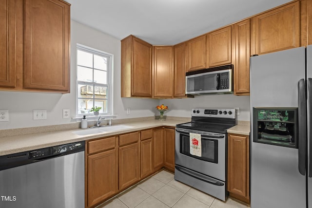 kitchen with brown cabinetry, a sink, light countertops, stainless steel appliances, and light tile patterned flooring