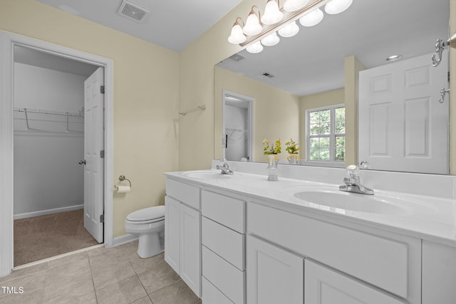bathroom featuring a sink, a walk in closet, toilet, and visible vents