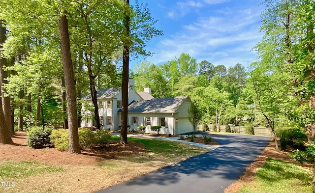 view of front of property featuring an attached garage, a chimney, and aphalt driveway