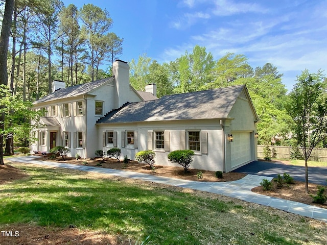 view of front of property with a front lawn, fence, a chimney, an attached garage, and driveway