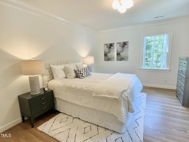 bedroom with baseboards, ornamental molding, wood finished floors, and visible vents