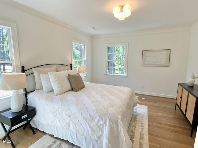 bedroom with crown molding, baseboards, light wood finished floors, and visible vents