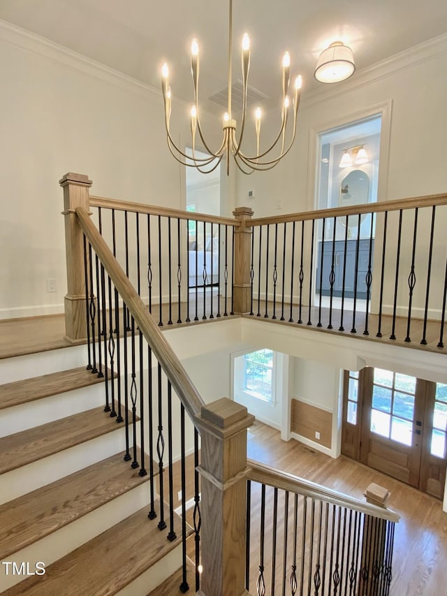 stairway with crown molding, wood finished floors, and an inviting chandelier