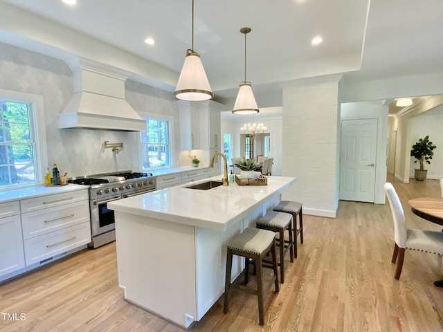 kitchen with a sink, light countertops, a center island with sink, double oven range, and custom exhaust hood