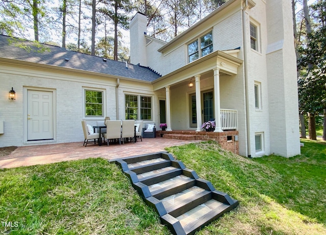 rear view of property with brick siding, a patio area, a yard, and a chimney