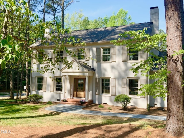 colonial inspired home with a chimney and a front lawn