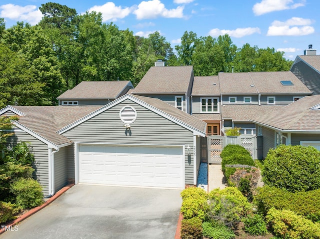 view of front facade featuring roof with shingles, an attached garage, a gate, a chimney, and driveway