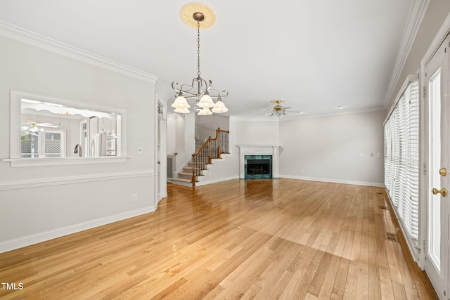 unfurnished living room featuring light wood-style floors, a premium fireplace, ceiling fan with notable chandelier, baseboards, and ornamental molding