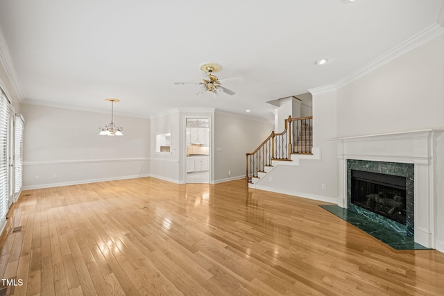 unfurnished living room featuring visible vents, stairway, light wood-type flooring, a high end fireplace, and ceiling fan with notable chandelier