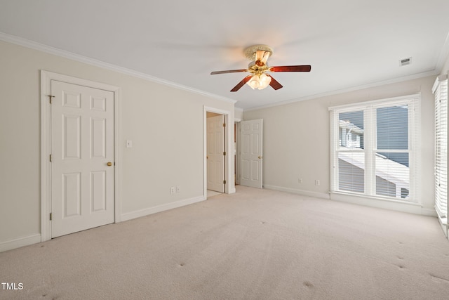 carpeted spare room featuring crown molding, baseboards, ceiling fan, and visible vents