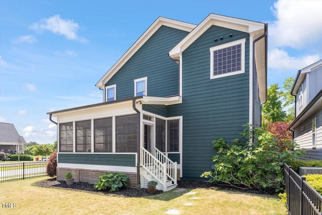 rear view of property with a lawn, fence, and a sunroom