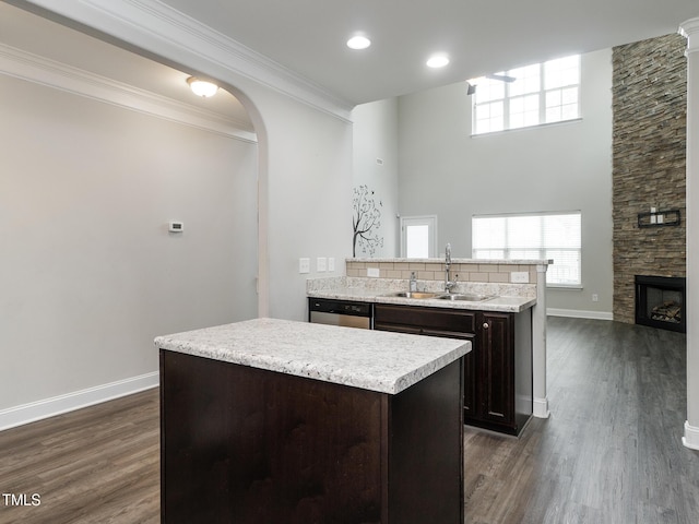 kitchen featuring a sink, dark wood-style flooring, stainless steel dishwasher, a kitchen island, and dark brown cabinets