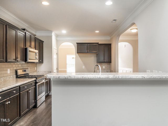 kitchen with arched walkways, crown molding, appliances with stainless steel finishes, and dark brown cabinetry