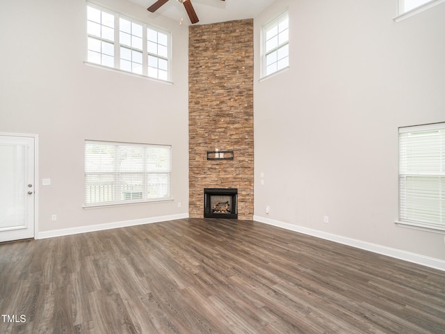 unfurnished living room featuring a ceiling fan, a fireplace, dark wood-type flooring, baseboards, and a towering ceiling
