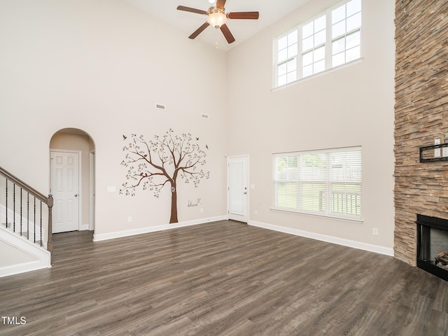 unfurnished living room featuring a ceiling fan, a stone fireplace, dark wood finished floors, and high vaulted ceiling