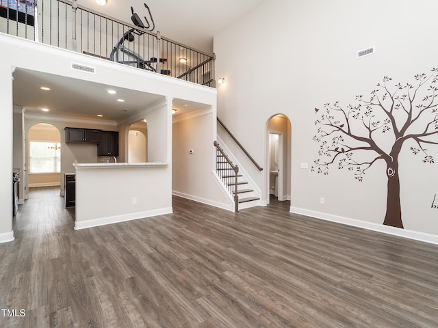 unfurnished living room featuring visible vents, stairway, a towering ceiling, arched walkways, and dark wood-type flooring