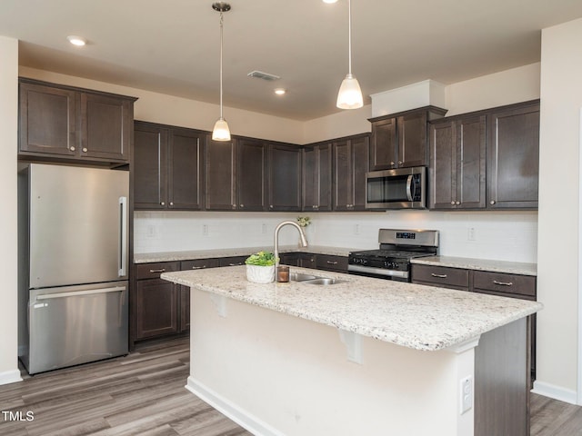 1218 S Franklin St, Wake Forest, NC 27587 - kitchen featuring stainless steel appliances, dark brown cabinets, light wood-style floors, an island with sink, and tasteful backsplash