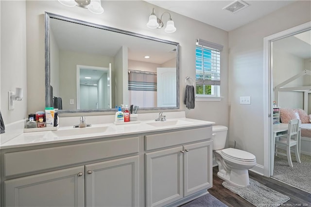 6528 Carswell Dr, Fayetteville, NC 28311 - bathroom featuring visible vents, double vanity, wood finished floors, toilet, and a sink