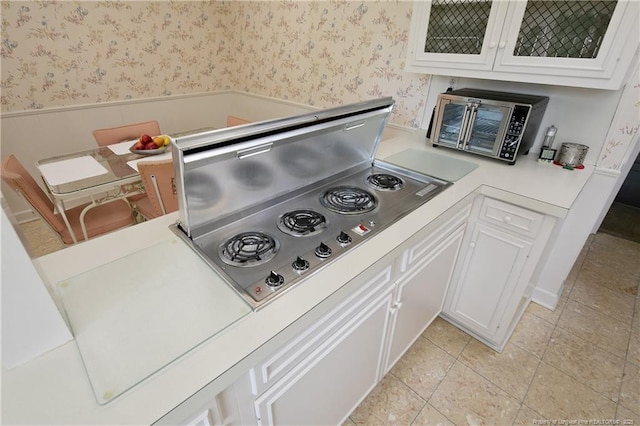 details featuring wainscoting, light countertops, white cabinetry, wallpapered walls, and glass insert cabinets